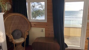 Ein gemütlicher Raum mit einem Korbstuhl, einer kleinen Holzbank, einem Fenster mit Meerblick und einer Heizung.
