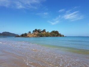 Una playa con aguas cristalinas, una orilla arenosa y una pequeña isla con árboles.