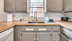A kitchen with grey cabinets, a wooden countertop, a sink, and a window with a view of the outside. - Oasis in Central Oklahoma City (Oklahoma City)