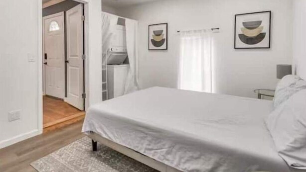 A modern bedroom with a bed, a small bedside table, and a window with curtains. - Oasis in Central Oklahoma City (Oklahoma City)