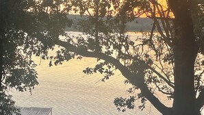 Vista de un lago con un muelle, sillas y un árbol.