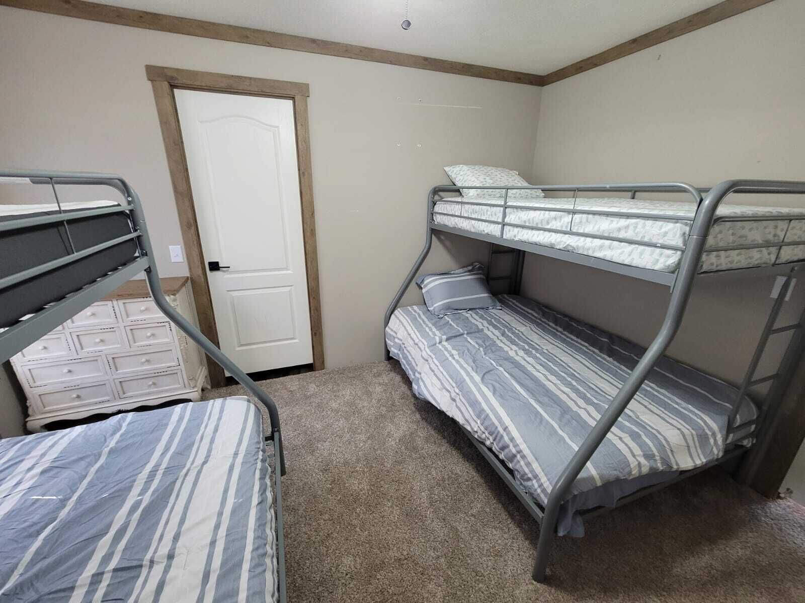 A dormitory room with bunk beds, a door, and a small dresser.