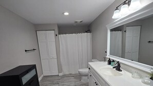 Un baño con tocador blanco, espejo, inodoro y cortina de ducha.
