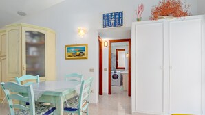 A dining area with a table and chairs, a kitchen in the background, and a wardrobe.