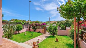A courtyard with a stone pathway, a wooden fence, and a variety of plants and flowers.