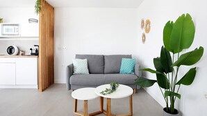 A modern living space with a grey sofa, wooden sideboard, white round tables, and a large green plant. - Holiday Home 'Casa Adriana' with Private Pool, Wi-Fi and Air Conditioning (Conil de la frontera)