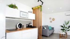 A modern kitchen with a microwave, coffee maker, and wooden accents, a grey sofa with a plant, and a small table with a plant. - Holiday Home 'Casa Adriana' with Private Pool, Wi-Fi and Air Conditioning (Conil de la frontera)