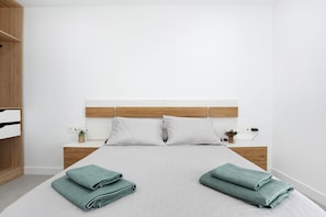 Un lit bien fait, avec une tête de lit blanche, deux oreillers et des serviettes pliées posées sur le lit.