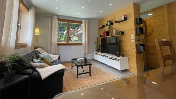 Ein modernes Wohnzimmer mit Sofa, Couchtisch, Fernseher und Holzregalen.