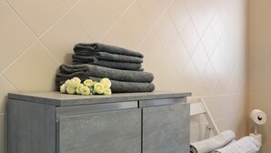Une salle de bain avec un meuble de couleur grise, un porte-serviettes sur lequel sont pliées des serviettes, et un porte-rouleau de papier toilette.