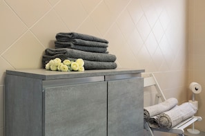 Une salle de bain avec un meuble de couleur grise, un porte-serviettes sur lequel sont pliées des serviettes, et un porte-rouleau de papier toilette.