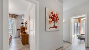 Un couloir avec un banc en bois, un tableau représentant des fleurs et un lit en arrière-plan.