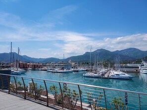 Un port de plaisance avec des bateaux amarrés, un ciel dégagé et des montagnes en arrière-plan.