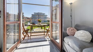 Un balcon avec une table et des chaises, un canapé avec des coussins et une vue sur les bâtiments.