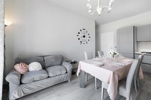 Un salon moderne avec un canapé gris, une table à manger dressée pour quatre personnes et une cuisine en arrière-plan.