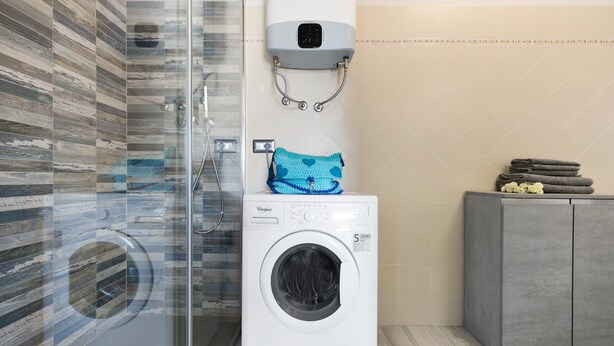 Ein moderner Waschraum mit einer Frontlader-Waschmaschine und -trockner, einer Glasdusche und einem grauen Schrank mit Handtüchern.