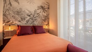 A bed with an orange bedspread, two purple pillows, and a wall mural of tropical foliage. - LE Pinot - Porte-de-savoie (PORTE-DE-SAVOIE)