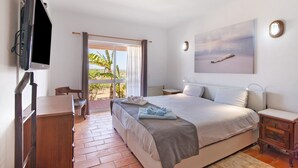 Une chambre à coucher comprenant un lit, un bureau, une chaise, un téléviseur et une fenêtre avec des rideaux.