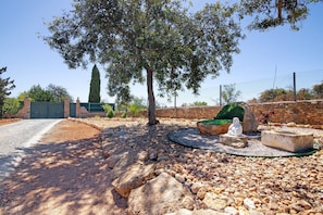 A landscaped outdoor area with a stone wall, a large tree, and a statue.