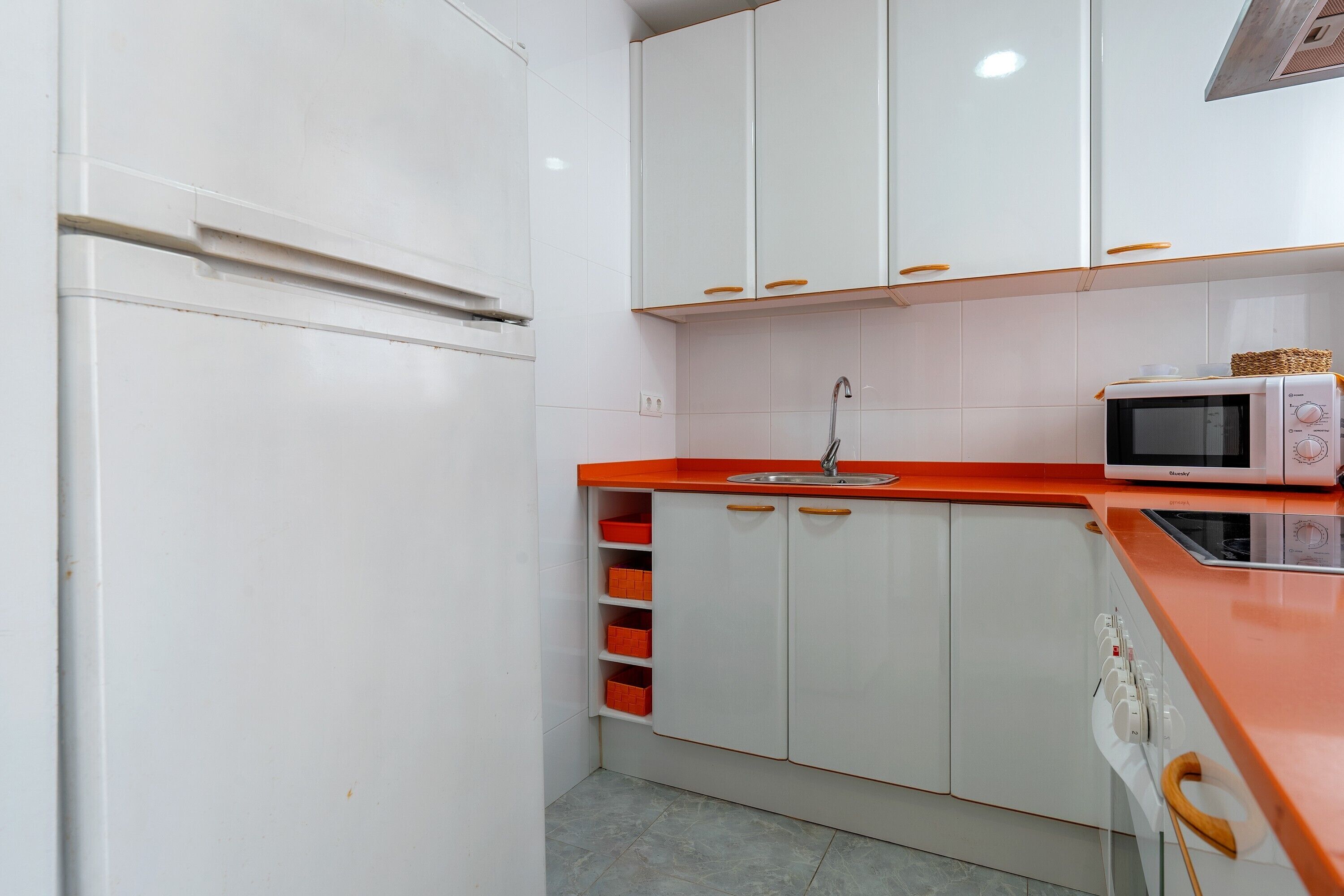 A kitchen with white cabinets, a red countertop, a microwave, and a sink.