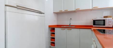 A kitchen with white cabinets, a red countertop, a microwave, and a sink.