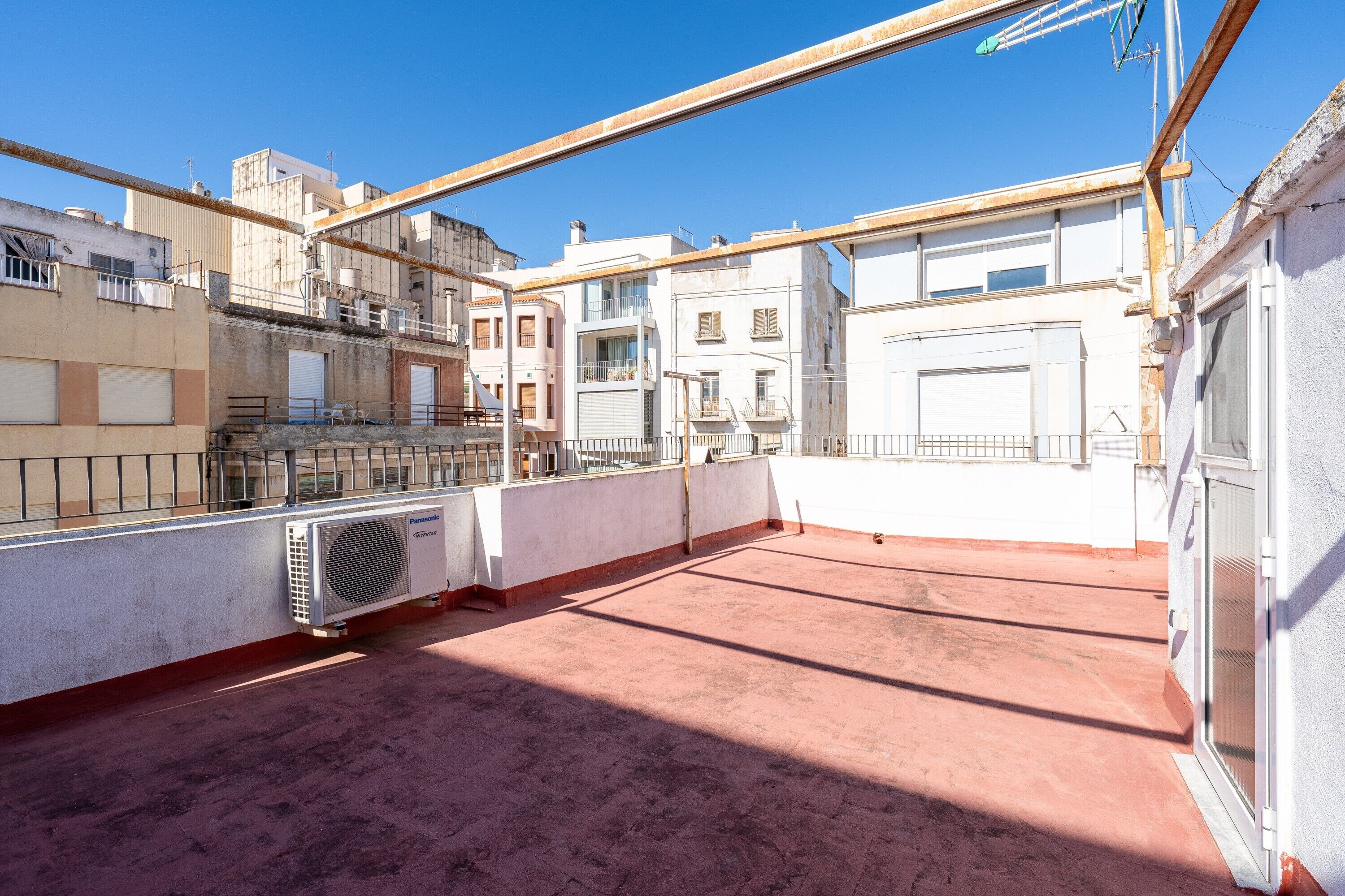 Terraza en la azotea con vistas a edificios circundantes, baranda metálica y un equipo de aire acondicionado grande.