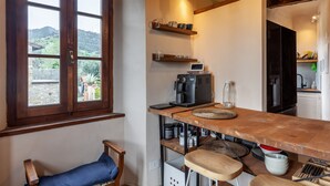 Une cuisine équipée d’une machine à café, de plusieurs étagères où sont rangées des tasses, d’un ordinateur et offrant une vue sur l’extérieur.