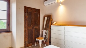 Une pièce avec une porte en bois, une chaise blanche, une commode blanche et un appareil de climatisation.