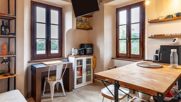 Une cuisine de taille réduite, dotée de meubles en bois, d’une table à manger et d’un téléviseur fixé au mur.