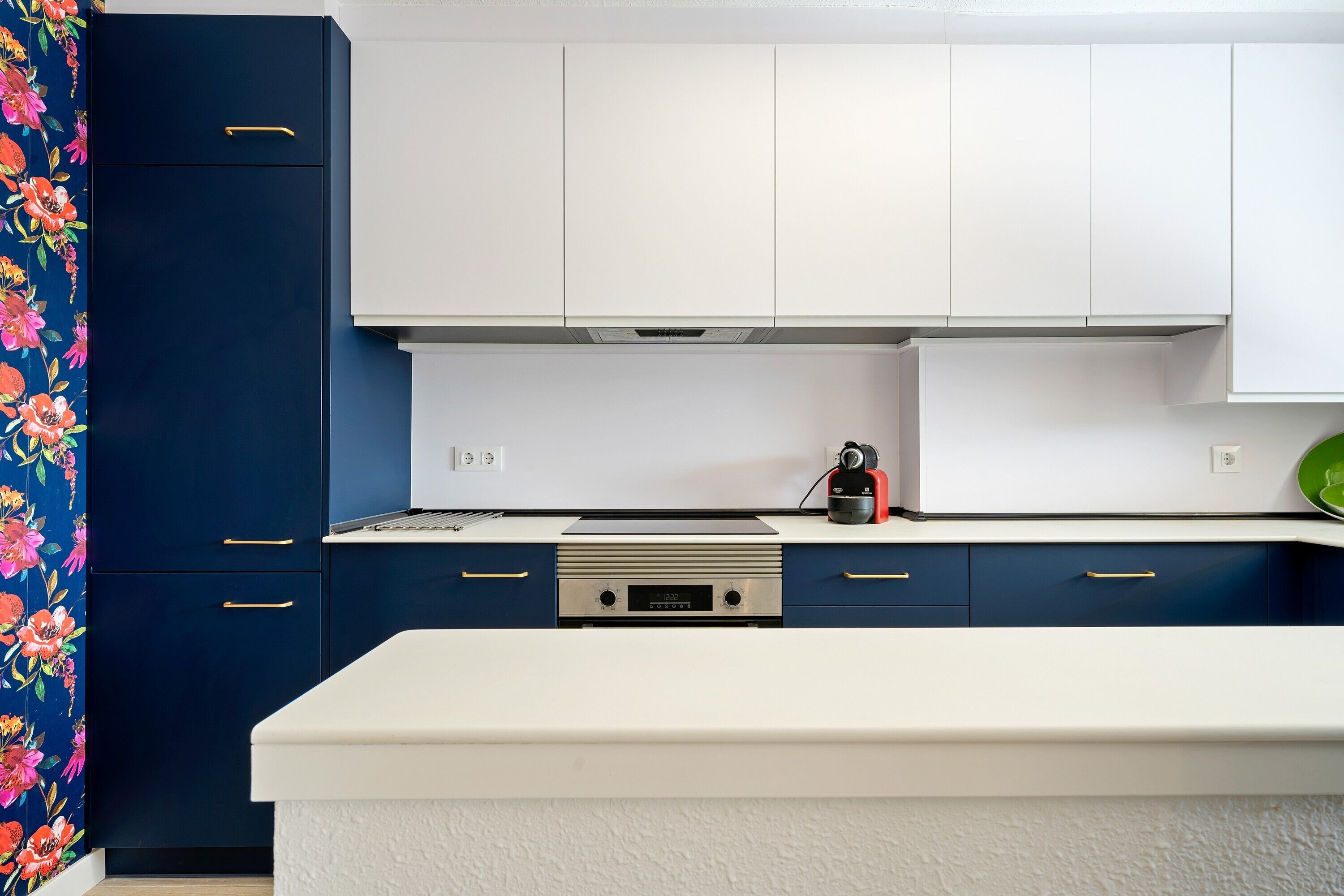 A kitchen with white cabinets, a blue countertop, and a floral-patterned curtain.