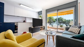 Un salon moderne avec un canapé, un fauteuil jaune, un téléviseur et un balcon doté d’un auvent jaune.