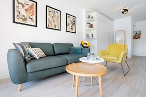 Ein modernes Wohnzimmer mit einer Couch, einem gelben Sessel, einem runden Holztisch und einer weißen Schrank mit Regalen.