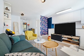 Ein modernes Wohnzimmer mit einer Couch, einem gelben Sessel, einem runden Holztisch und einer TV-Konsole mit einem Flachbildfernseher.