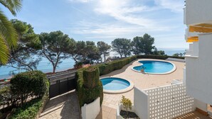 Un espace piscine comprenant deux piscines, entouré de verdure et offrant une vue sur la mer.