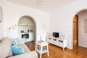 Una sala de estar moderna con un sofá, televisión y una pequeña mesa. Cuenta con una zona de cocina con armarios y estufa.