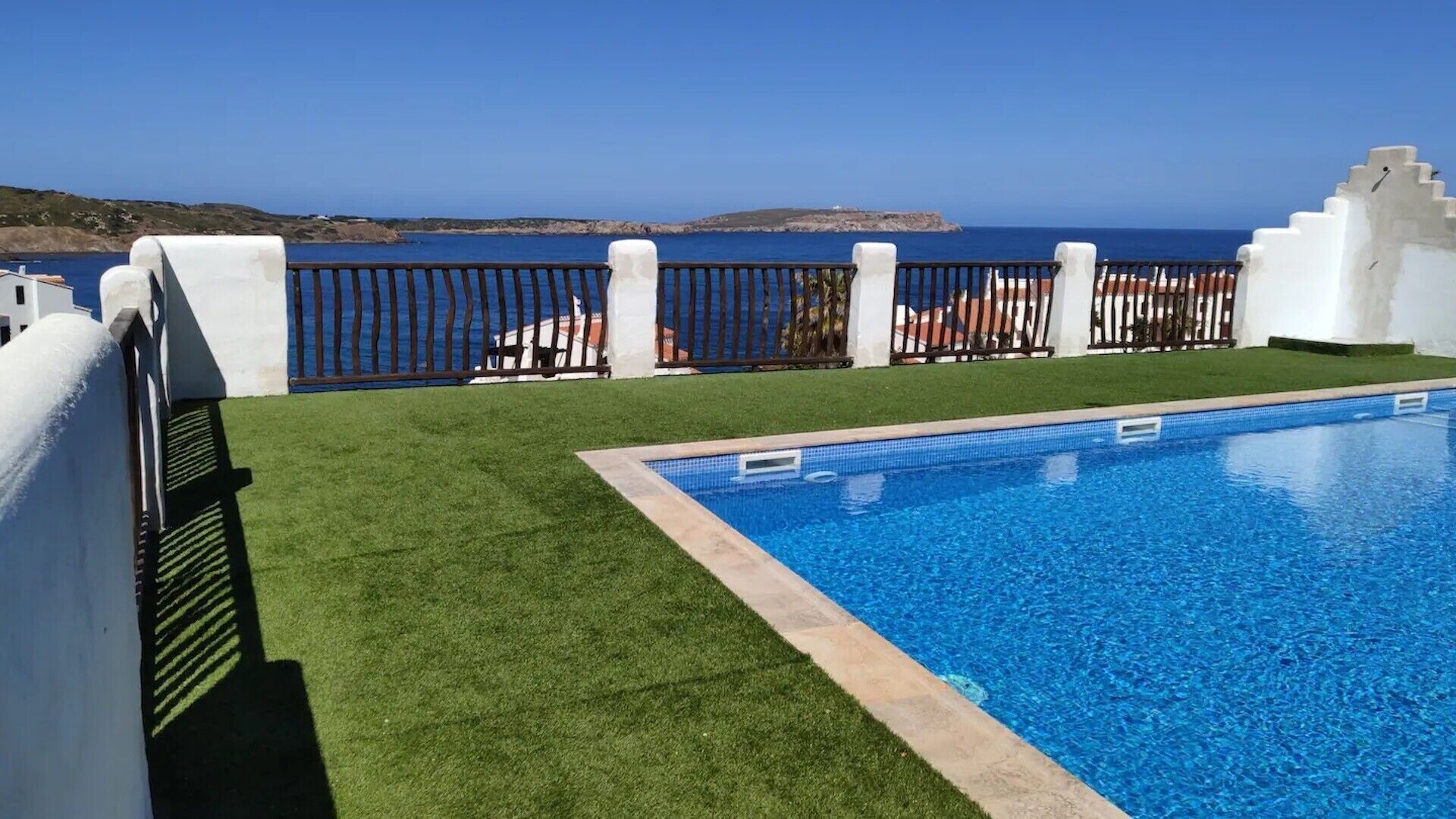 Una piscina con vista al mar, rodeada de paredes blancas y una cerca de metal.