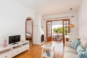 Una sala de estar con televisor, sofá y chimenea. Hay un comedor con mesa y sillas.