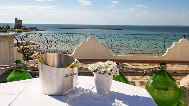A table with a metal bucket, a vase with flowers, and a green bottle.