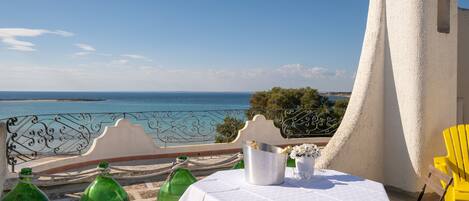 A terrace with a table set for dining, overlooking a coastal view.