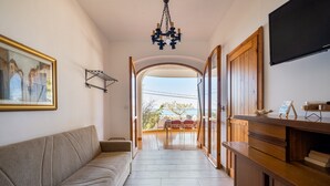 A hallway with a sofa, a chandelier, a TV, and an open door leading to a balcony.