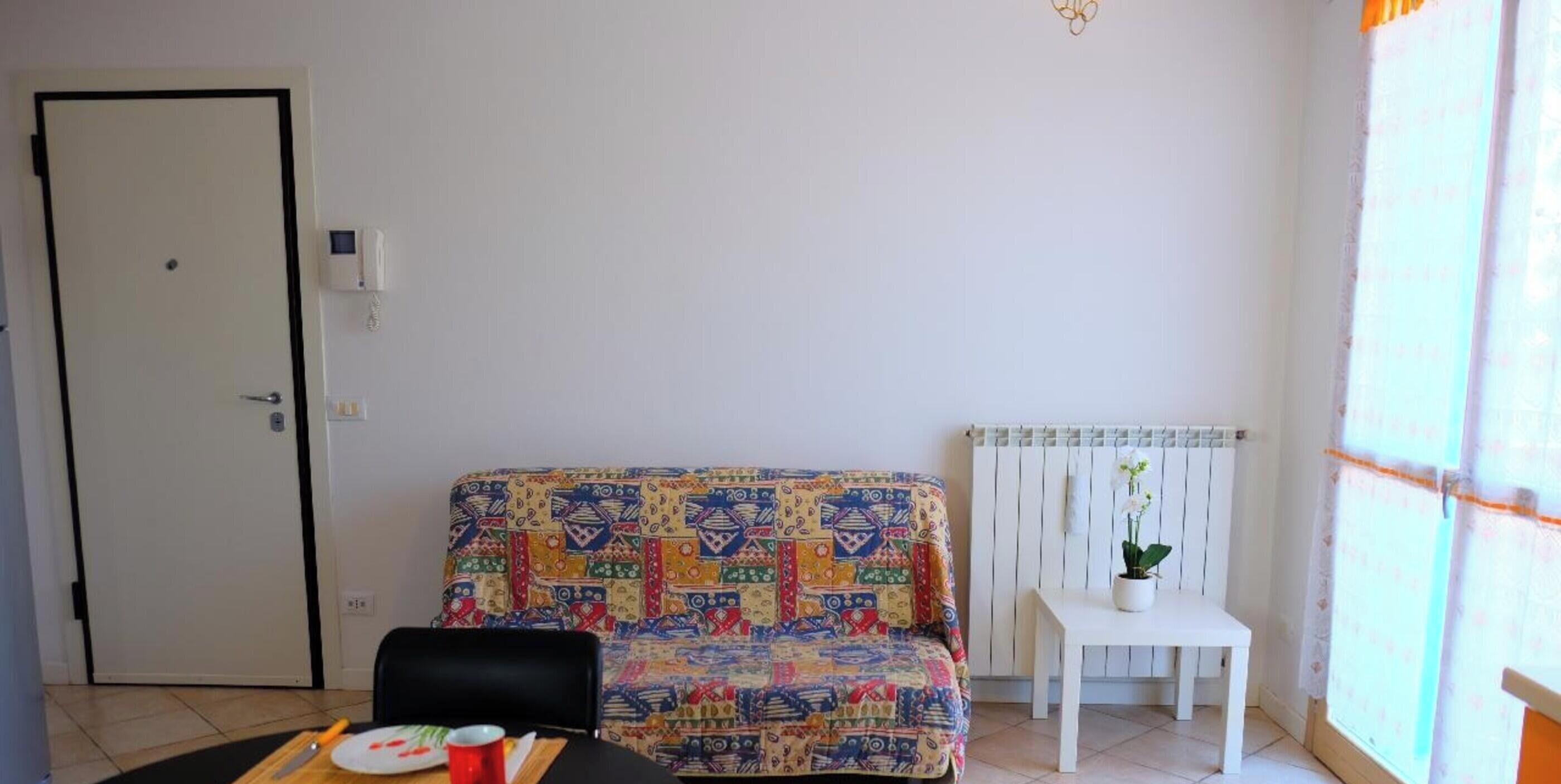 Una habitación con un sofá estampado, una mesita con una planta en maceta, una puerta y un radiador.