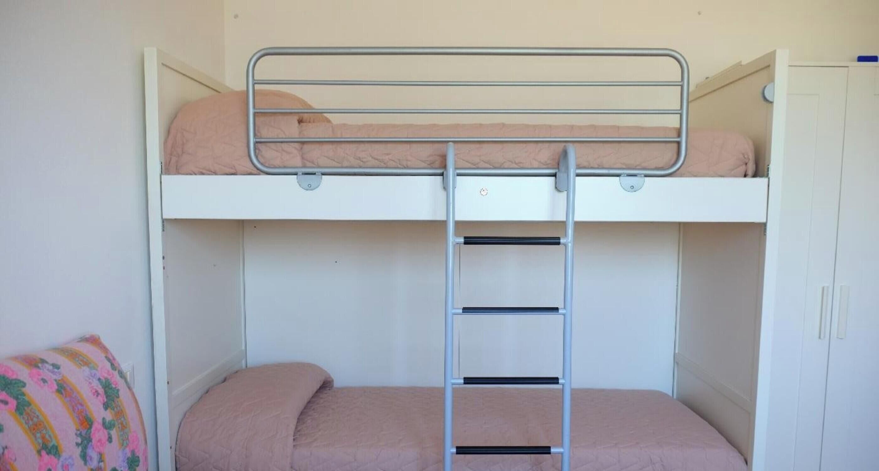 A bunk bed with a ladder, a white wardrobe, and a floral pillow on the lower bunk.