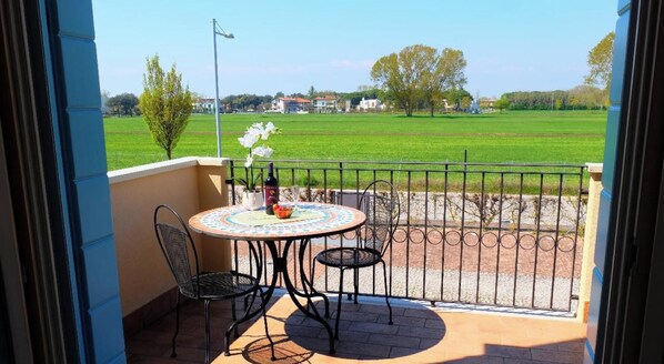 A balcony with a table and chairs, a potted plant, and a bottle of wine. - Apartment 'Residence Borgo Dei Fiori D03' with Shared Pool, Private Terrace and Air Conditioning (Jesolo)