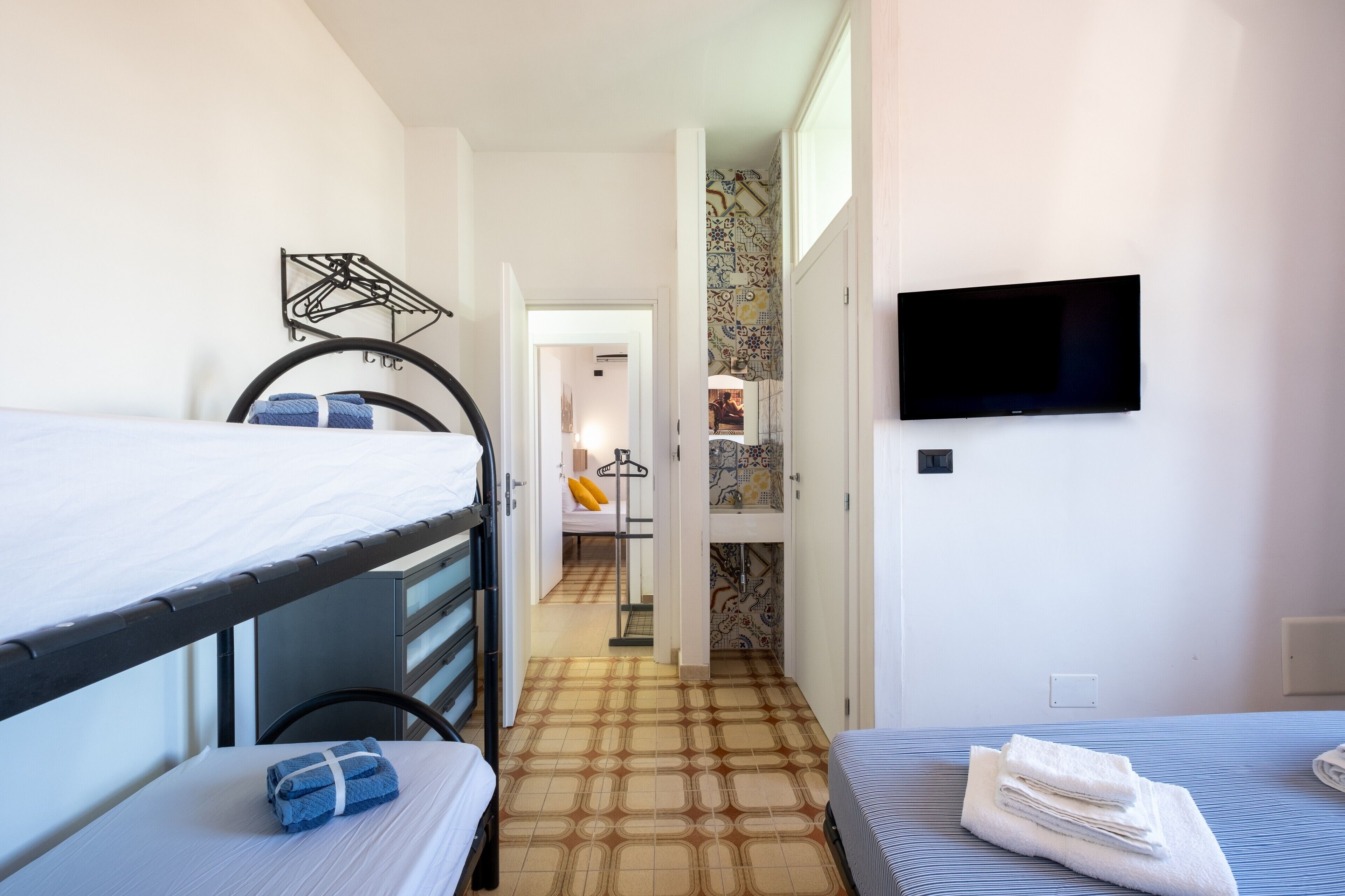 Una habitación con literas, televisión, suelo estampado y un pasillo que conduce a otra habitación.