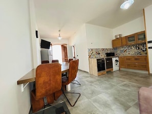 A compact kitchen with a dining area, a washing machine, and a TV mounted on the wall.