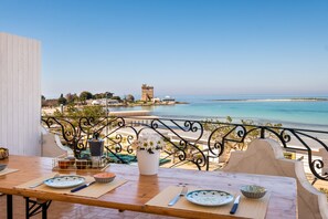 A balcony with a table set for dining, overlooking a beach and a tower.