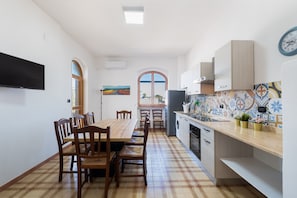 A kitchen with a tiled floor, wooden dining table, chairs, and cabinets.