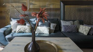 Una sala de estar con un sofá azul oscuro, cojines estampados y un jarrón con flores sobre una mesa de centro de madera.