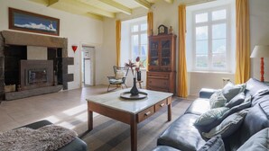 Una sala de estar con chimenea, un sofá, una mesa y un ventanal con cortinas.