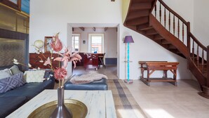 Amplia sala de estar con sofá, una mesa de centro, un jarrón con flores, una escalera y vista a la cocina.